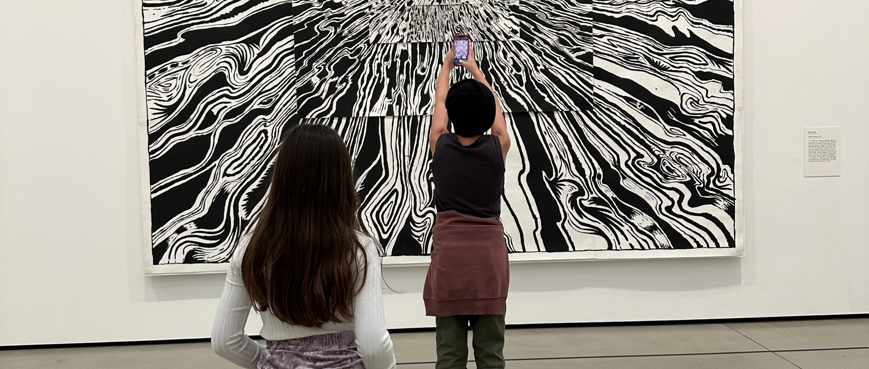 Two children photographing a large black-and-white painting